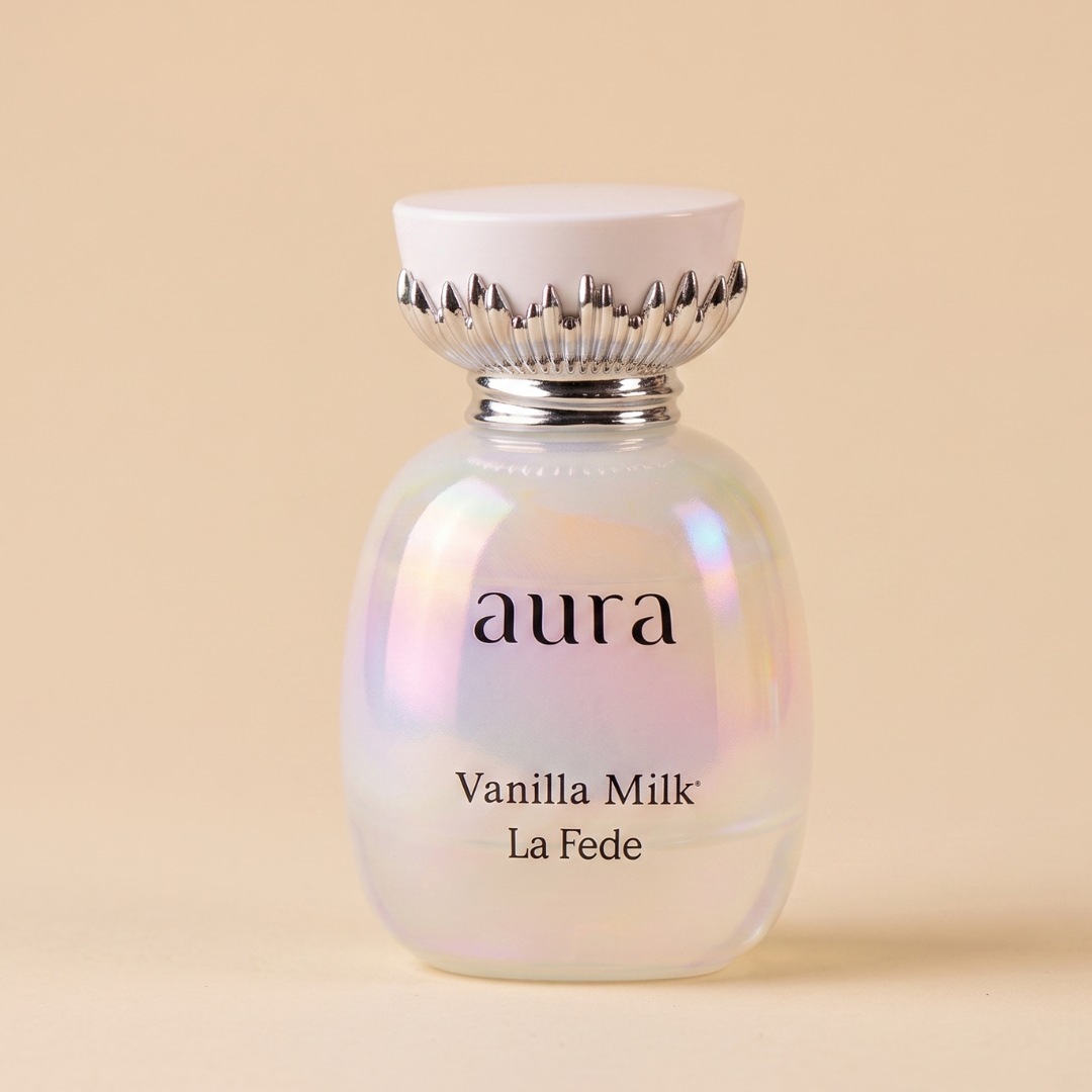 A shimmering perfume bottle with a white cap and silver details, labeled "Aura Vanilla Milk 100ml EDP - Khadlaj," is set against a beige background, evoking the creamy woody essence of this fragrance from Khadlaj.