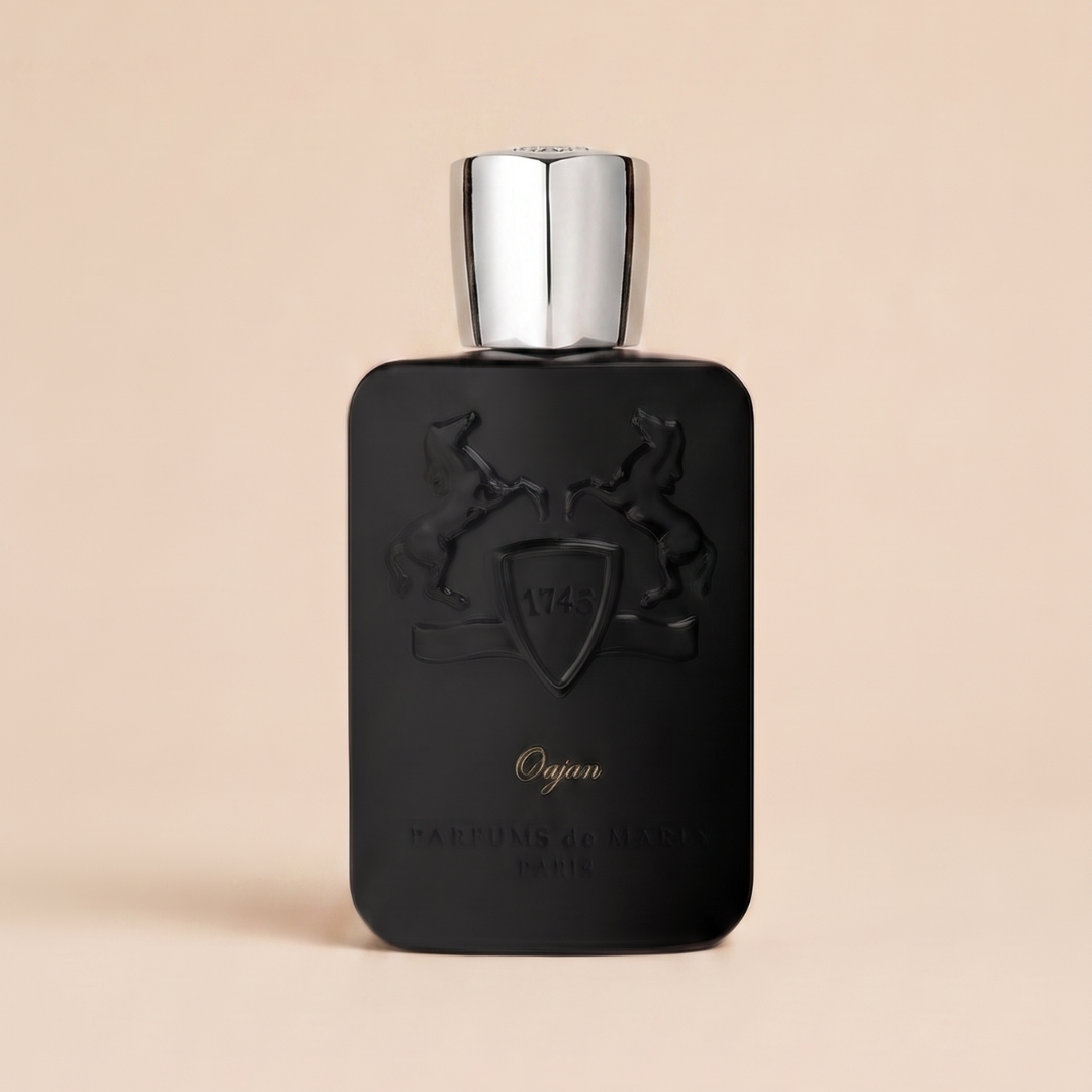 A matte black bottle of Oajan 120ml EDP by Parfums De Marly features a silver cap and is embossed with two rearing horses flanking a shield marked "1743," while the fragrance name, "Oajan," appears below in gold lettering. Set against a soft beige backdrop, this elegant design perfectly echoes the warmth and richness of its signature amber scent from Parfums De Marly.