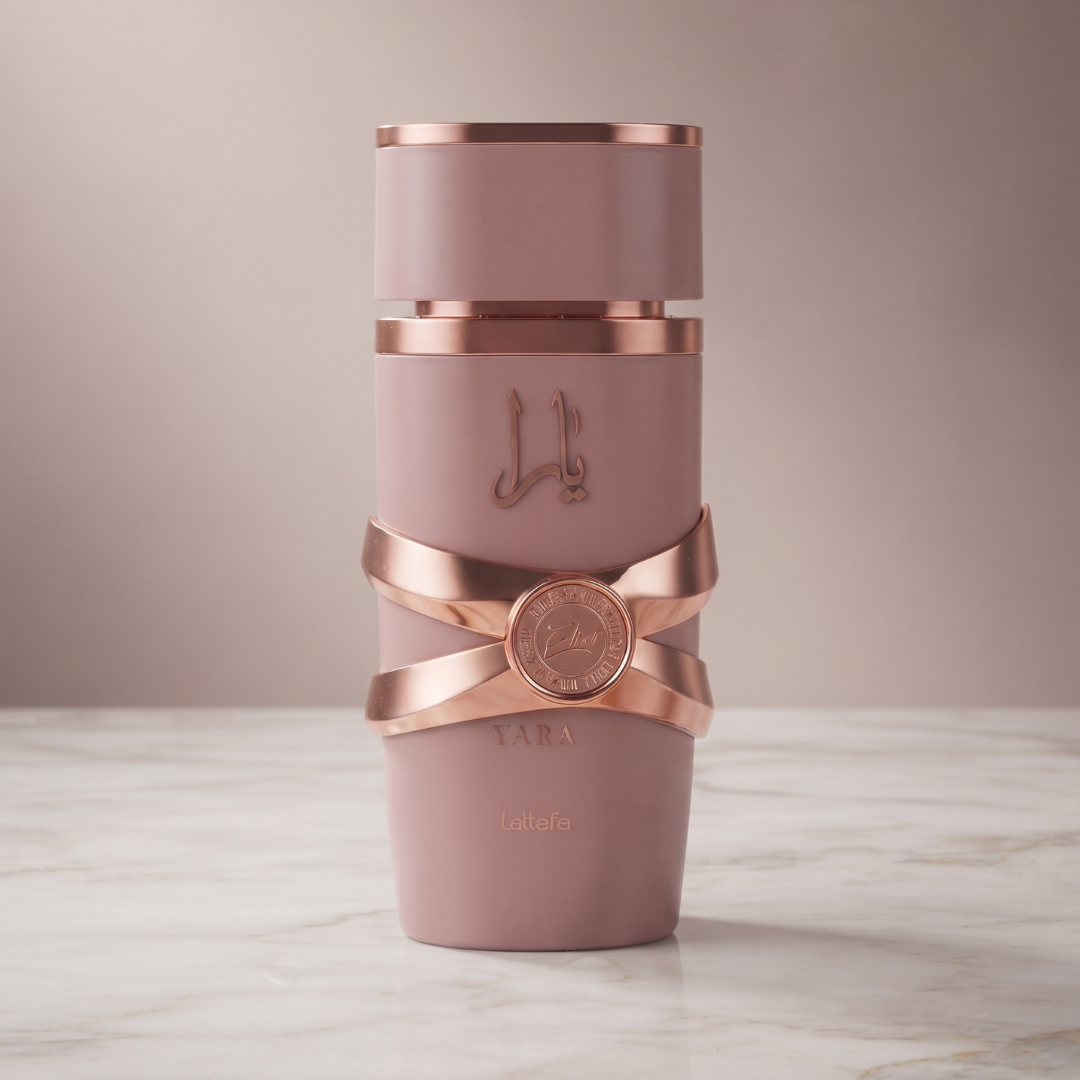A pink bottle adorned with rose gold accents, Arabic script, and the word “YARA” sits elegantly on a white marble surface against a neutral background—an eye-catching display for Yara Elixir 100ml EDP by Lattafa, the sweet gourmand fragrance from Lattafa.