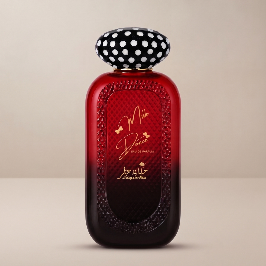 A vibrant red bottle of Mille Douce 100ml EDP by Hekayat Attar, featuring a textured surface, elegant gold lettering, and a distinctive black-and-white polka dot cap, is displayed against a neutral background to beautifully evoke the creamy fruity gourmand character of this signature fragrance.