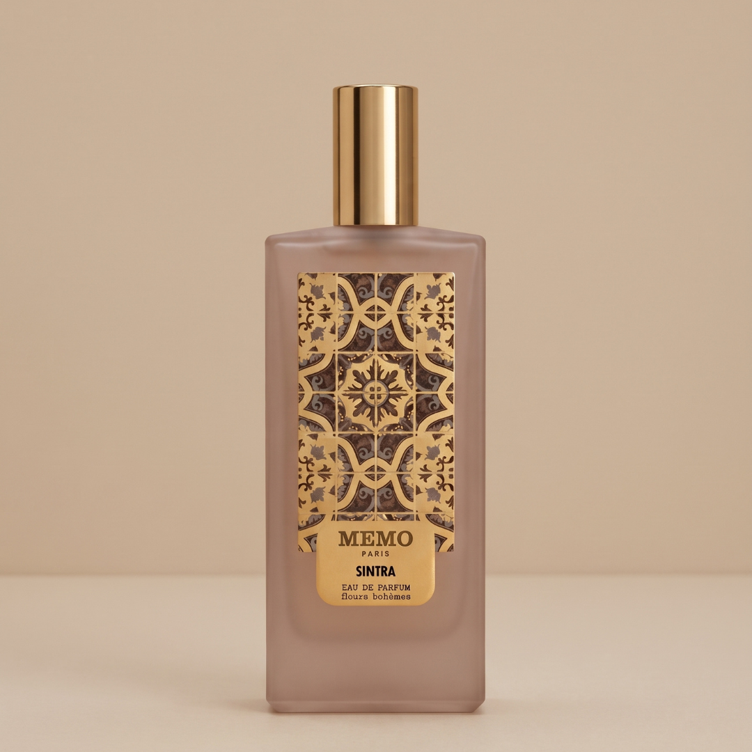 A rectangular 75ml bottle of Memo Paris Sintra Eau de Parfum, featuring a gold cap and ornate gold label, is displayed against a beige background—evoking the luxurious orange blossom and caramel vanilla notes of this signature fragrance from Memo Paris.