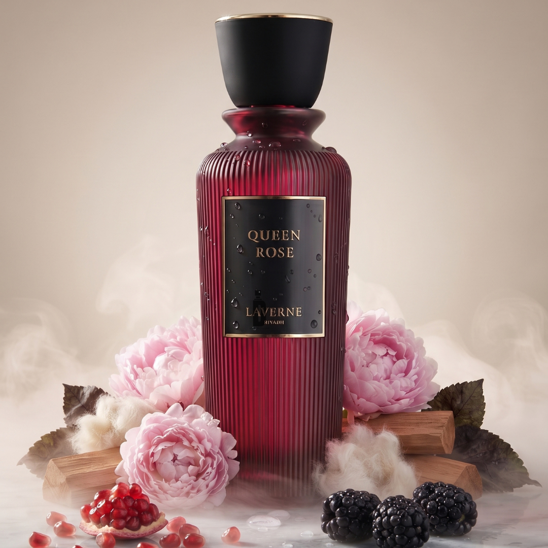 A striking red bottle of Laverne’s Queen Rose 200ml EDP is showcased amid delicate pink flowers, luscious blackberries, pomegranate seeds, and pieces of sandalwood, all draped in a soft mist on a neutral backdrop—capturing the enchanting allure of this floral fragrance elegantly blended with subtle sandalwood notes.