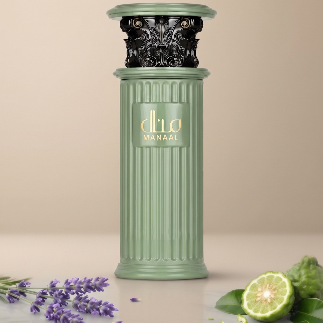 A tall, mint-green bottle of Manaal 100ml EDP by Ard Al Zaafaran stands with an ornate black top, gold “dlia MANAA” label, and carved vertical lines. Fresh lavender sprigs and a sliced lime rest beside it on a beige surface, capturing the irresistible allure of this gourmand fragrance, which features tempting notes of decadent pistachio.