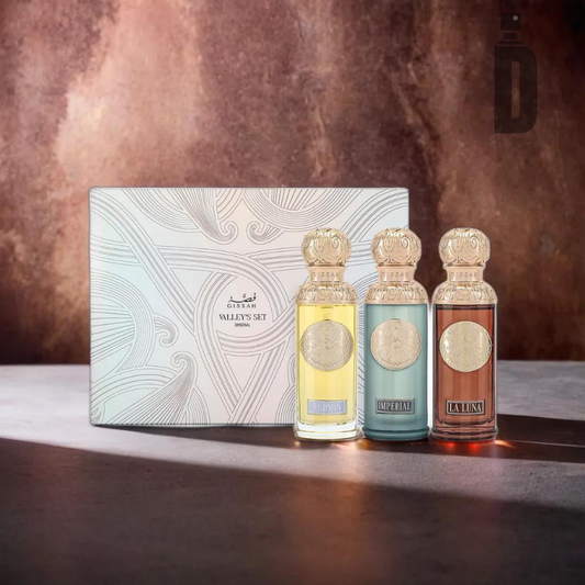 A luxurious collection of three elegant perfume bottles, each adorned with intricate gold caps, is showcased in front of a decorative box labeled "Valley's Set EDP 3x50ml - Gissah" by the prestigious brand Gissah. This exquisite fragrance set contains yellow, blue, and pink liquids, all offering delightful oriental woody undertones. The display is set against a richly textured brown background.