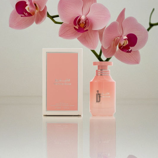 A Vanilla Rose 100ml EDP by Arabian Oud and its matching box are displayed with pink orchids on a light, reflective surface, creating an elegant scene that highlights this romantic Eau de Parfum fragrance.