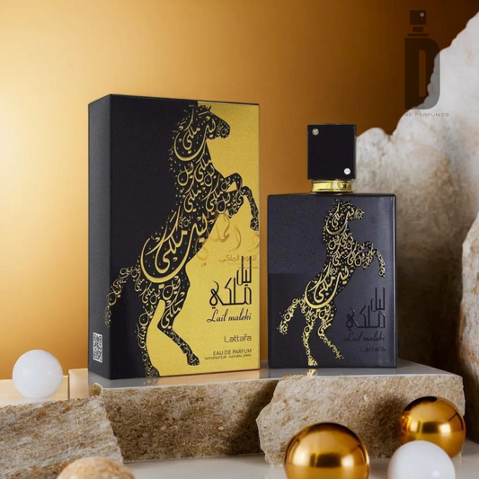 A black perfume bottle and its matching box, adorned with an elegant gold horse design and intricate patterns, are displayed on a rocky surface. The bottle and packaging, labeled "Lail Maleki 100ml EDP - Lattafa" by Lattafa, contain a seductive fragrance. White and gold spherical decorations are artfully placed around them.
