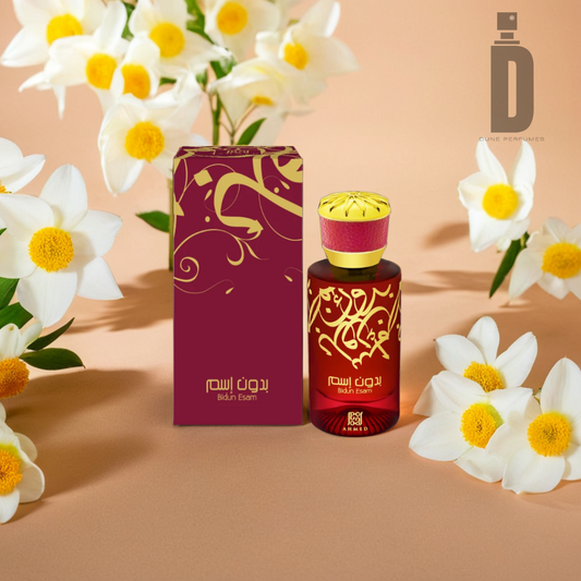 A bottle of Bidun Esam 50ml EDP by Ahmed Al Maghribi and its accompanying box are nestled among white and yellow flowers. Both the box and bottle are burgundy adorned with golden designs. The logo "I D" along with Arabic text is prominently displayed on the packaging, exuding an oriental charm. The backdrop features a light, warm shade.