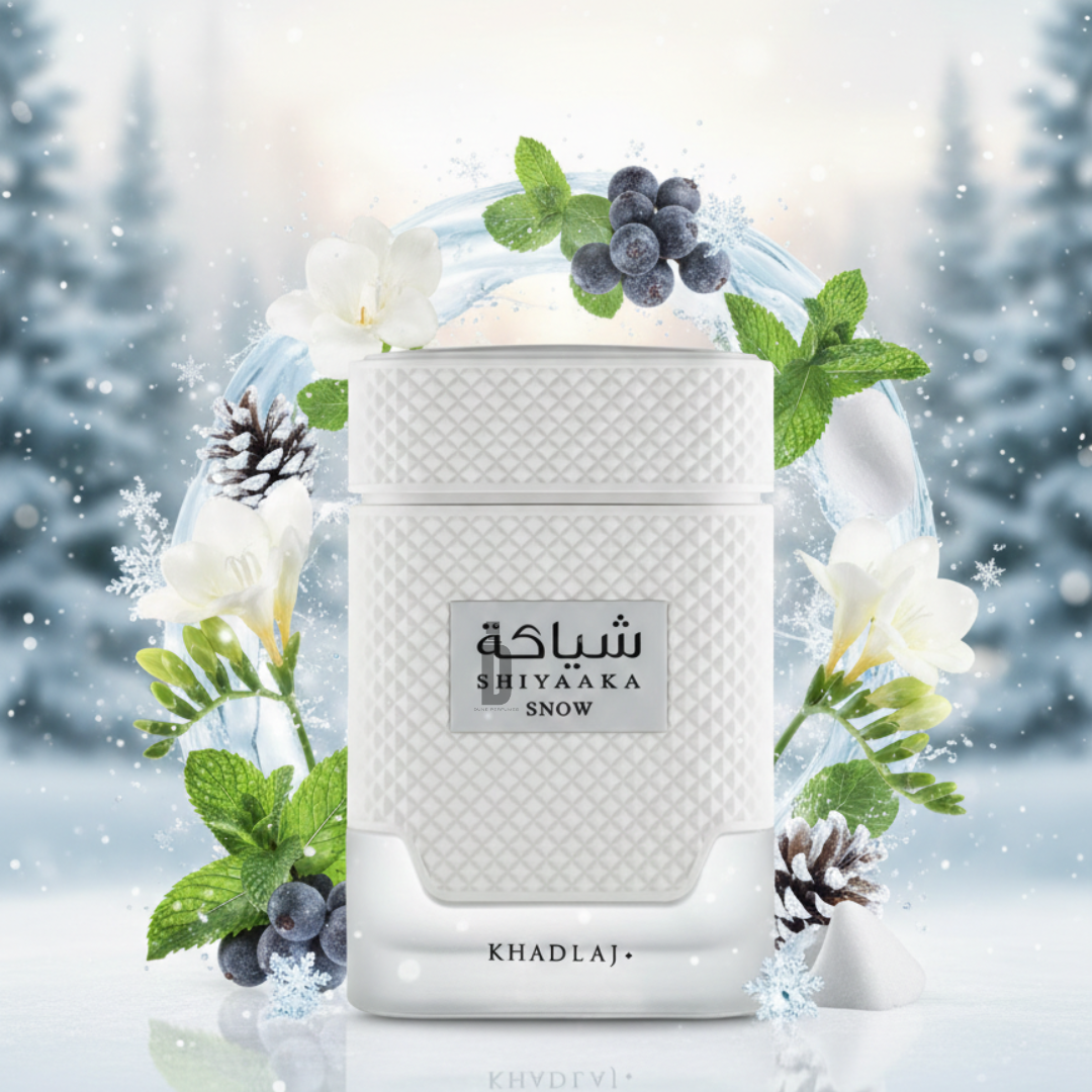 The Shiyaaka Snow 100ml EDP by Khadlaj features a white textured bottle, surrounded by mint leaves, white flowers, blueberries, and snow, suggesting a fresh, cool fragrance inspired by a frosty winter scene.