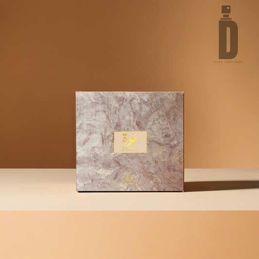 A square, beige marbled box featuring a yellow floral logo and Arabic text centered on the front sits on a smooth, light brown surface with a matching brown backdrop. Infused with the rich aroma of bakhoor, the 'Marrah Bakhoor (6 tablets)' by Ahmed Al Maghribi logo is displayed in the top right corner.