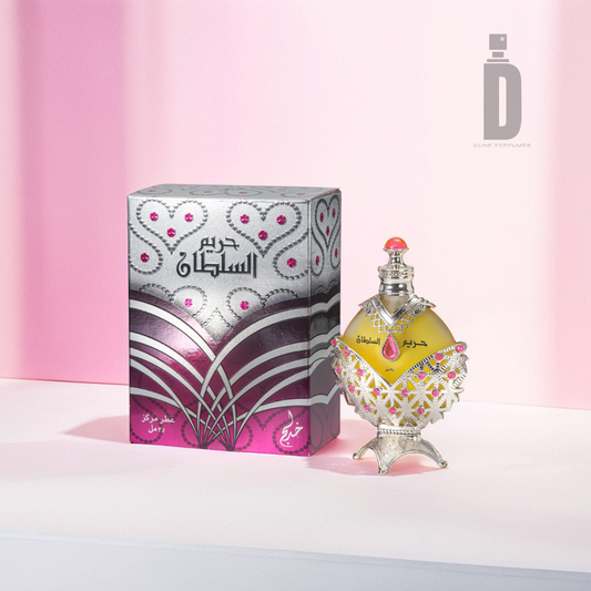 A beautifully designed Hareem Al Sultan Silver 35ml Perfume Oil by Khadlaj features intricate silver and pink patterns, accompanied by a matching box adorned with similar ornate designs. It is set against a soft pink background, creating an elegant display that embodies the essence of luxury fragrance.