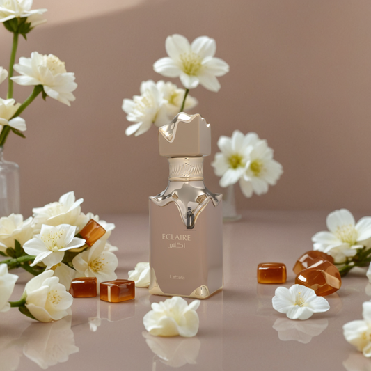 A gold Eclaire 100ml EDP bottle by Lattafa stands on a glossy surface, surrounded by white flowers, vanilla notes, and amber stones against a soft beige background.