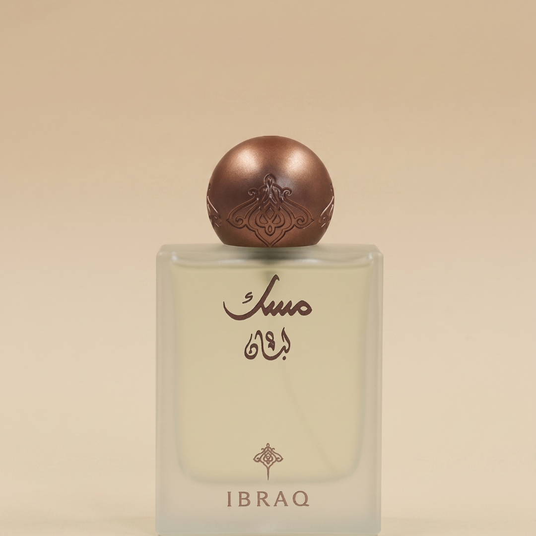 A square glass perfume bottle with brown Arabic script and a round metallic brown cap features "Musk Luban 75ml - Ibrahim Al Qurashi" by Ibrahim Al Qurashi, displayed against a soft beige gradient background.