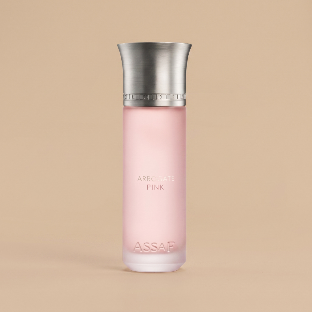 A tall bottle featuring pink frosted glass and a silver metallic cap, labeled “Arrogate Pink 200ml EDP - Assaf” at the base, stands against a beige background, perfectly capturing the elegance of this floral fragrance by Assaf.