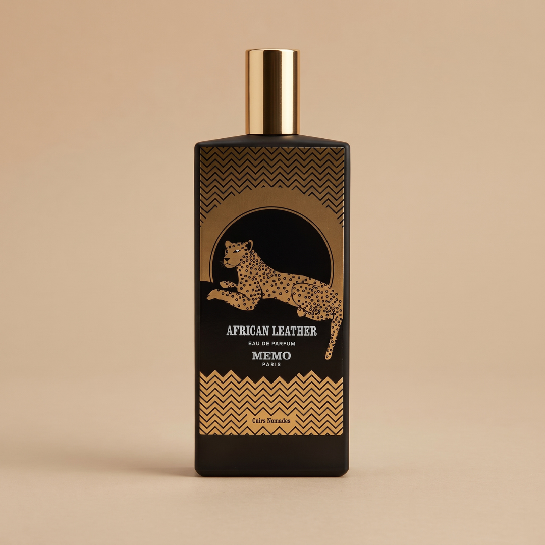 A black Memo Paris “African Leather 75ml EDP” perfume bottle, adorned with gold accents, geometric patterns, and a striking leopard illustration, stands upright on a beige background, capturing the exotic allure of this signature fragrance.