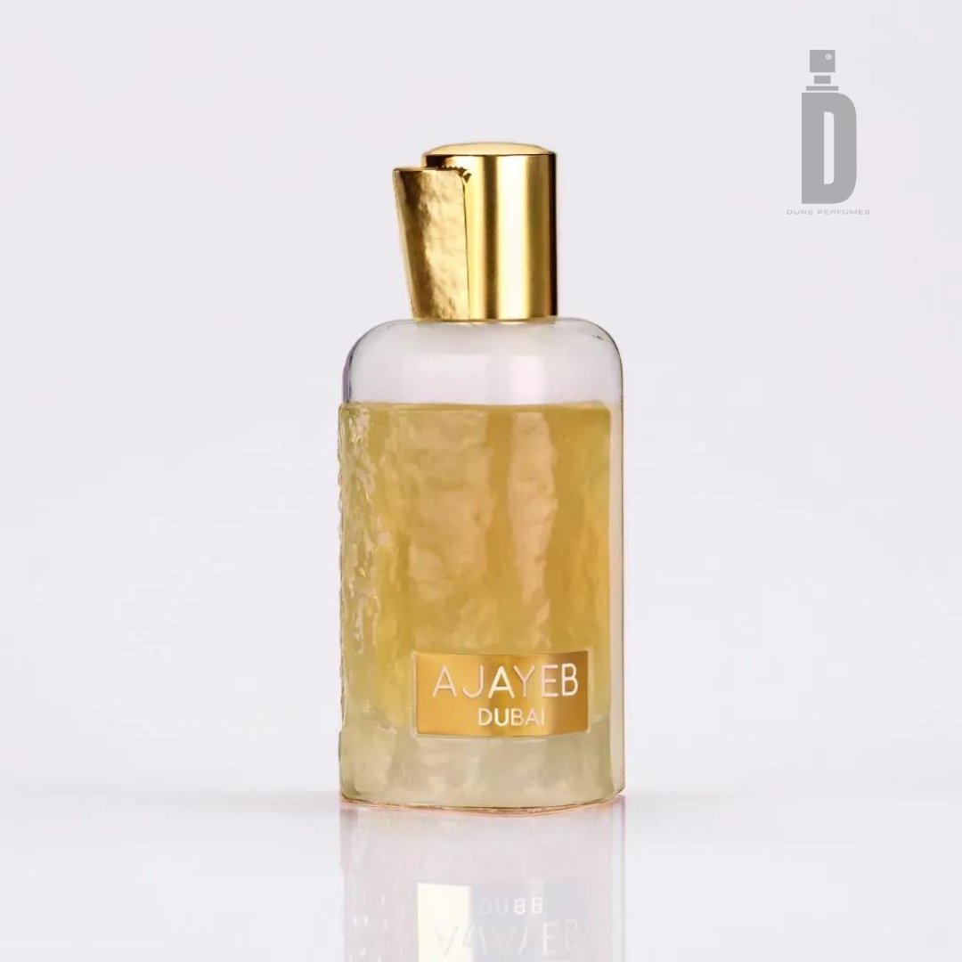 A bottle of Ajayeb Dubai Portrait 100ml EDP by Lattafa is celebrated for its luxurious fragrance featuring citrus top notes. The predominantly transparent bottle showcases a gold cap and a central label adorned with the name "AJAYEB DUBAI".