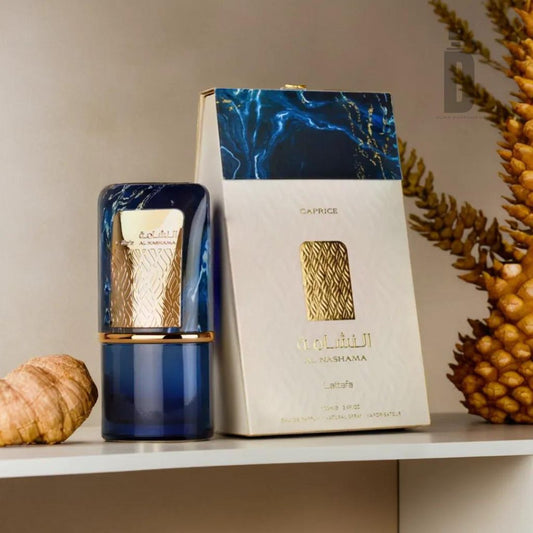 A bottle of Al Nashama Caprice 100ml EDP by Lattafa, renowned for its sophisticated scent and herbal freshness, is showcased next to its open packaging on a white shelf. The blue bottle with gold accents is complemented by decorative elements such as a pine cone and dried plant branches.