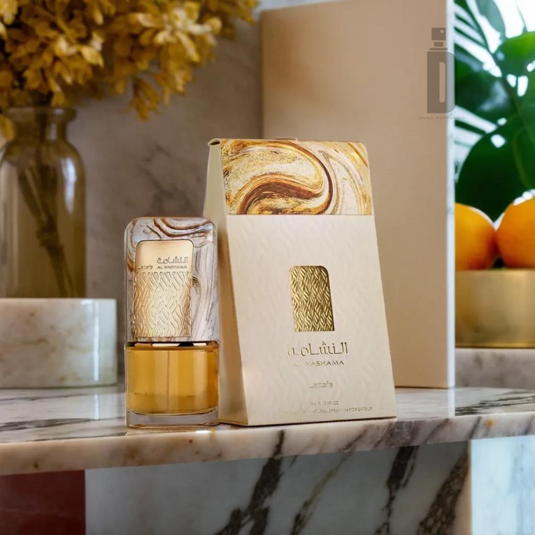 A sophisticated scent encased in an elegantly decorated bottle, Al Nashama Gold 100ml EDP by Lattafa, rests on a marble surface. The packaging, labeled "Al Nashama Gold," showcases intricate swirling gold and white designs. In the background, a vase with dried yellow flowers, a potted plant, and a bowl of oranges complete the luxurious scene.