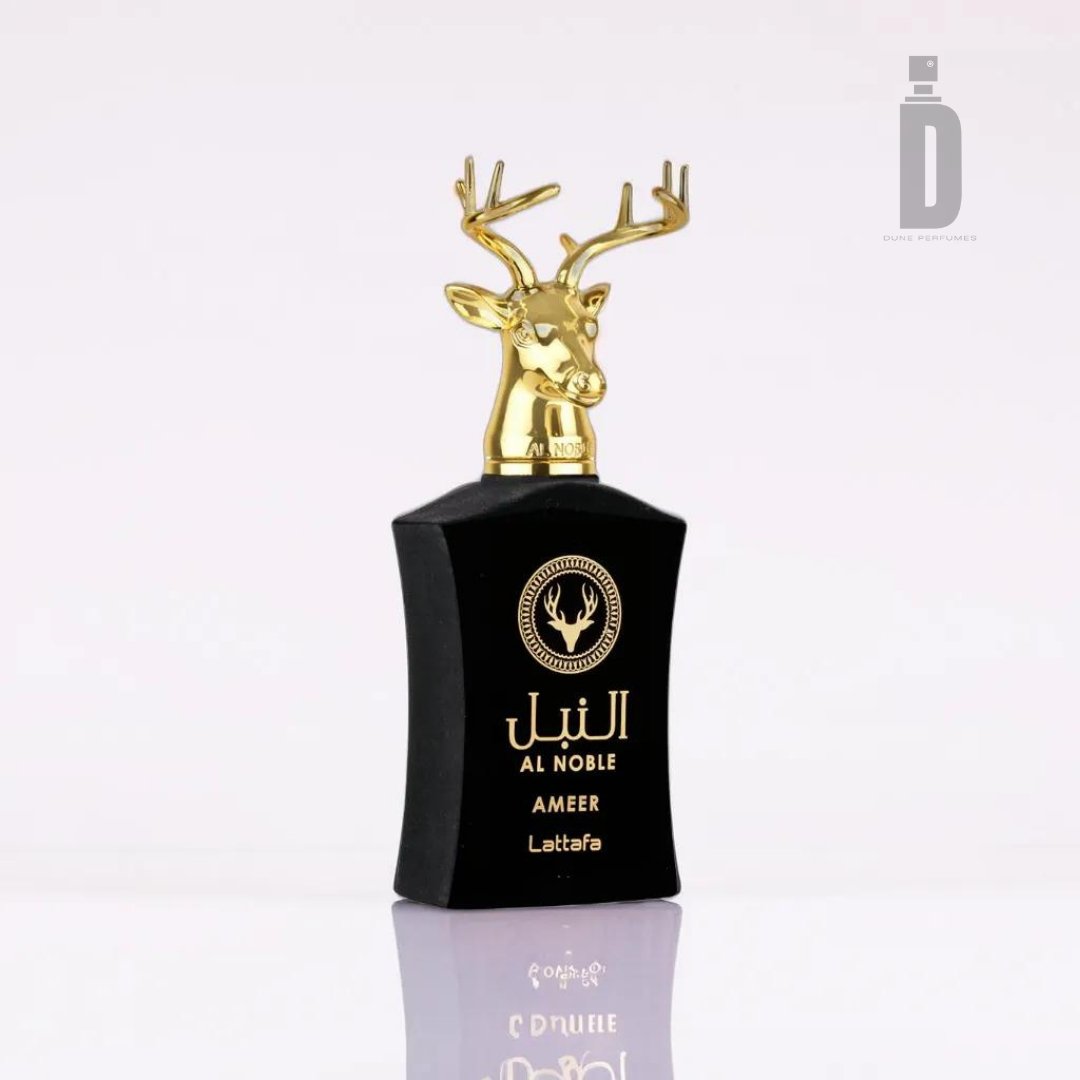 A black perfume bottle with a gold deer head as the cap. The front label reads "Al Noble Ameer 100ml EDP," "Ameer," and "Lattafa" with decorative elements and Arabic text. Infused with notes of oud and patchouli, the background is plain and light-colored.