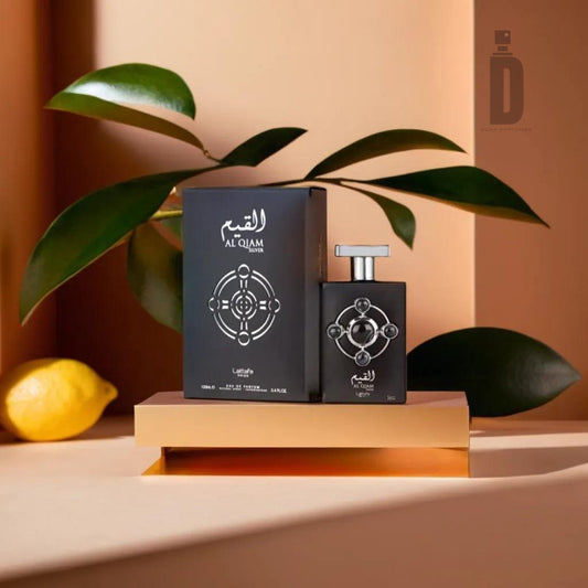 A bottle of Al Qiam Silver 100ml EDP by Lattafa Pride, featuring an intricate design, stands on a gold platform alongside its matching box. The setup includes green leaves and a yellow lemon in the background, providing a fresh and sophisticated presentation of the fragrance against a warm-toned backdrop.