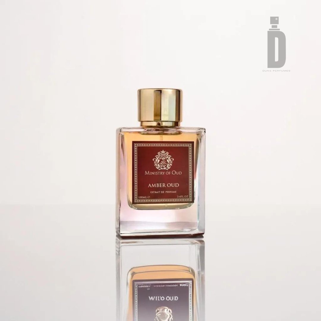 A bottle of "Amber Oud 100ml EDP - Ministry Of Oud" by Paris Corner is displayed against a light background. The rectangular bottle, embodying timeless allure, features a gold cap and a brown label with text. Its reflection shimmers on the glossy surface below, hinting at the luxurious fragrance within.