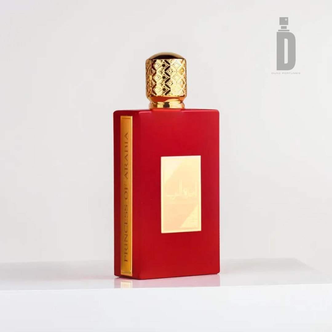 A vibrant red perfume bottle labeled "Ameerat Al Arab 100ml EDP - Asdaaf" by Lattafa, featuring a golden cap and a gold label on the front. The bottle, evocative of exotic oud, is set against a plain white background with a subtle, mirrored logo of "D" in the upper right corner.