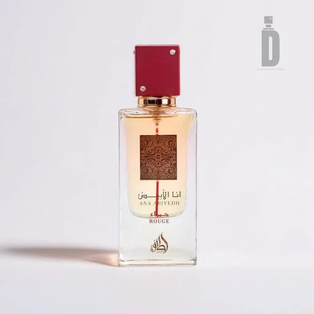 A clear glass perfume bottle with a red cap and a gold spray nozzle. The Lattafa Ana Abiyedh Rouge 60ml EDP features intricate gold and red designs, adorned with Arabic script and the words "Ana Abiyedh Rouge" below. This elegant fragrance hints at luxurious ambergris, set against a plain white background.