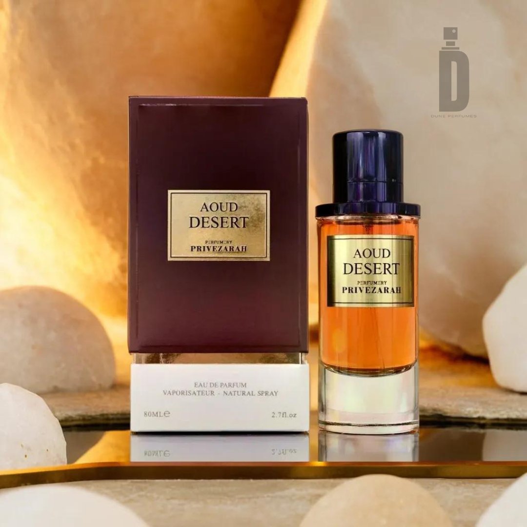 A bottle of Aoud Desert 80ml EDP by Paris Corner stands next to its packaging. The captivating fragrance is housed in an amber-colored bottle with a dark cap, and the box is brown with gold labeling. The background features soft lighting and smooth, rounded stones, evoking exotic landscapes.