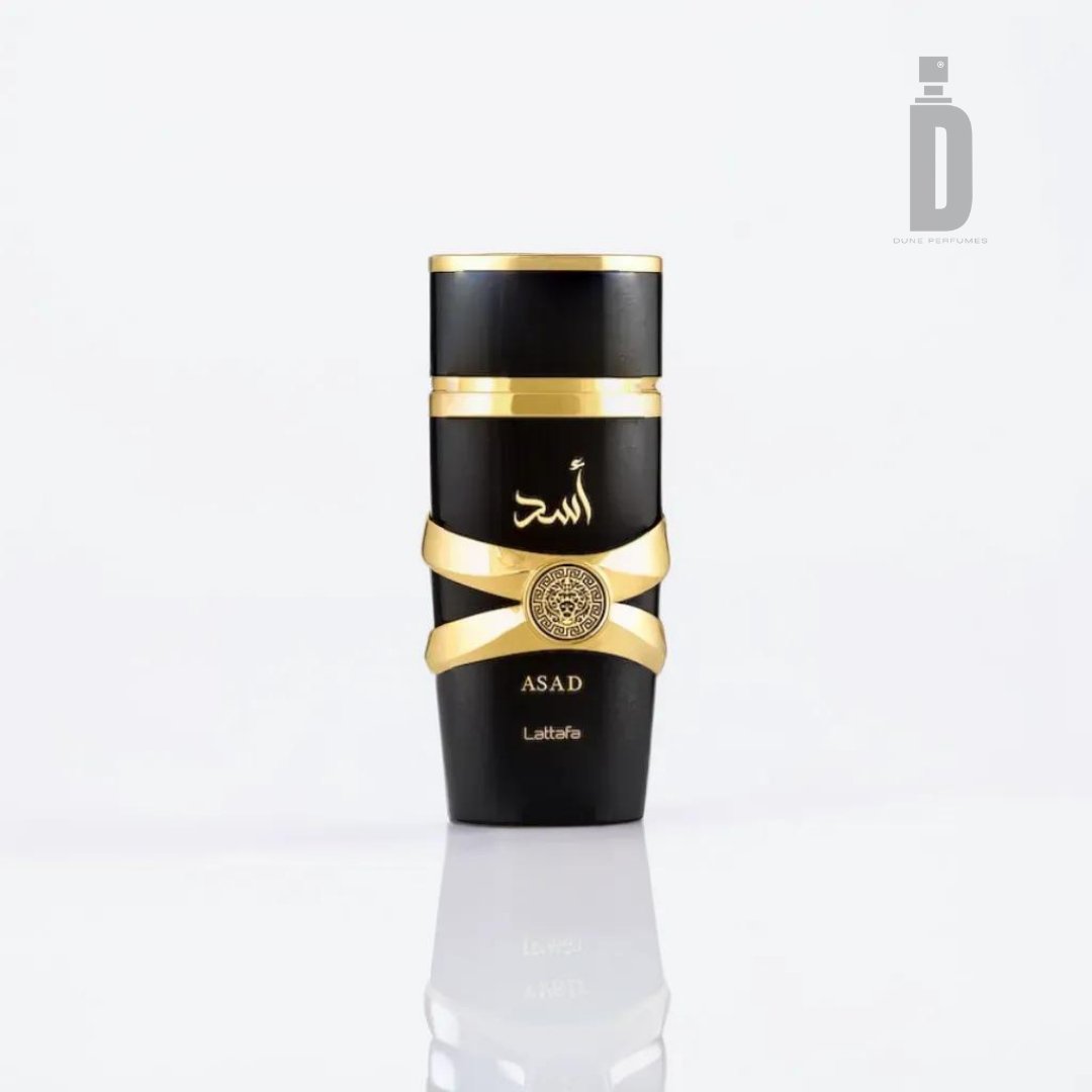 A black and gold perfume bottle labeled "Asad" in both Arabic and English. The design showcases gold accents and a central medallion, emphasizing the bold and spicy fragrance of Asad. The bottle's bottom features the brand name "Lattafa," all set against a plain white background.