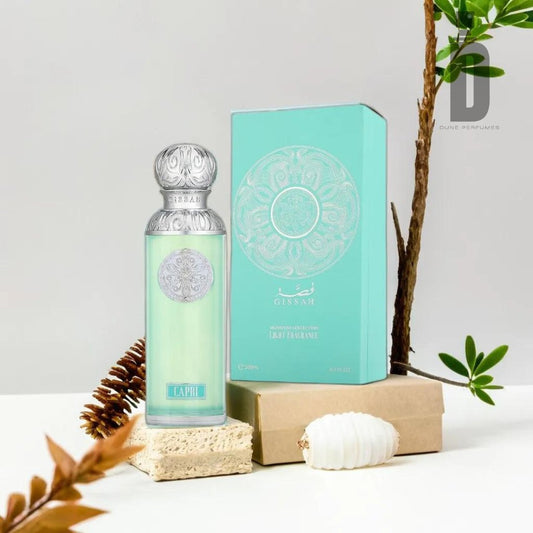 A perfume bottle and its box are displayed on top of stacked boxes with a pine cone and shell beside them. The bottle, featuring a silver ornate cap and a turquoise label reading "Capri 200ml EDP - Gissah," promises a dynamic fragrance. The intricately detailed turquoise box evokes a coastal escape, while a plant decorates the background.