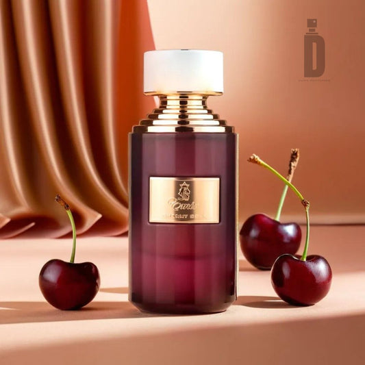 A luxurious bottle of Cherry Cola 75ml EDP by Paris Corner, adorned with a gold and white cap, is placed on a smooth surface. The bottle boasts a rich, dark reddish hue reminiscent of black cherry, with three cherries positioned around it. Silky, bronze-colored fabric drapes elegantly in the background.