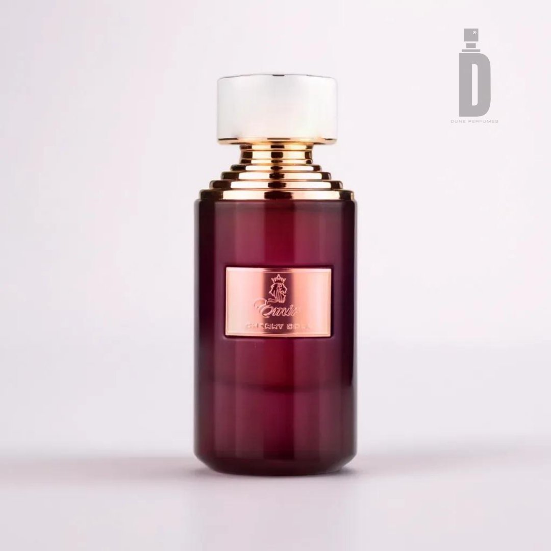 A luxurious perfume bottle with a deep maroon body and a shiny gold cap, the Cherry Cola 75ml EDP by Emir from Paris Corner features elegant typography and a crest-like emblem on its label. The fragrance exudes notes of black cherry, blending seamlessly into the sophisticated background gradient of white to light pink.