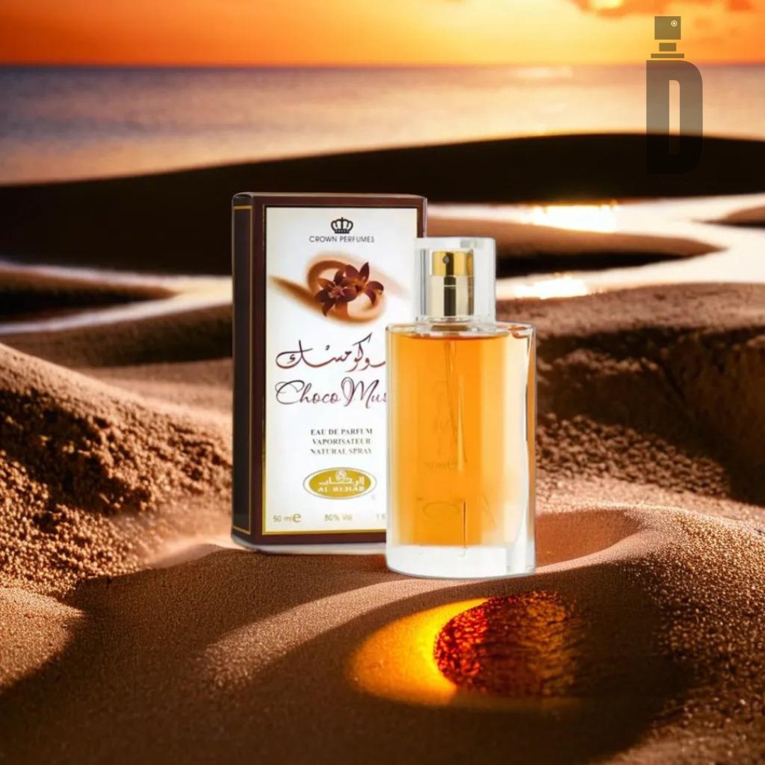 A bottle of Choco Musk by Al Rehab is nestled next to its box on the golden sand dunes, where sunlight casts a warm glow over the desert landscape, enhancing the musky essence and hint of chocolate that linger enticingly in the air.