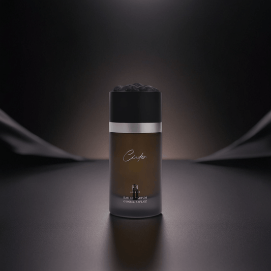 A sleek, dark perfume bottle labeled “Cinder 100ml EDP - Ahmed Al Maghribi” stands centered on a smooth, dark surface, radiating smoky elegance under soft, dramatic lighting with a blurred, shadowy background.