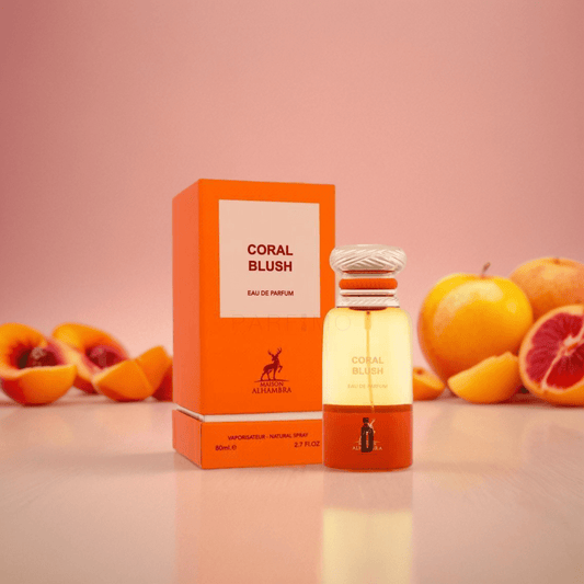A bottle and box of Coral Blush 80ml EDP by Maison Alhambra are shown on a pink surface, with peach, blood orange, and patchouli notes in the background against a soft pink backdrop.