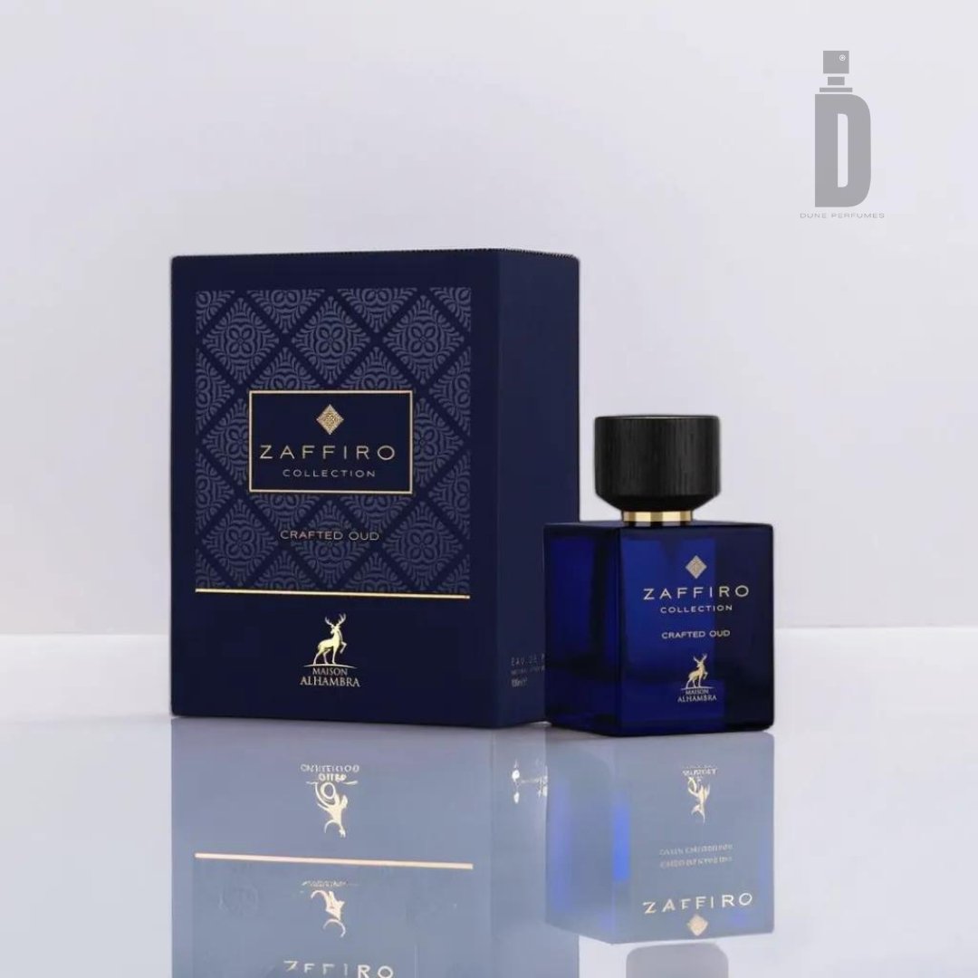 The image showcases a sophisticated fragrance product from Maison Alhambra, featuring a blue bottle labeled "Crafted Oud 100ml EDP - Maison Alhambra" with a black cap, alongside a matching blue and gold box. Both items are displayed on a reflective surface, with the faint logo of Maison Alhambra visible in the background.