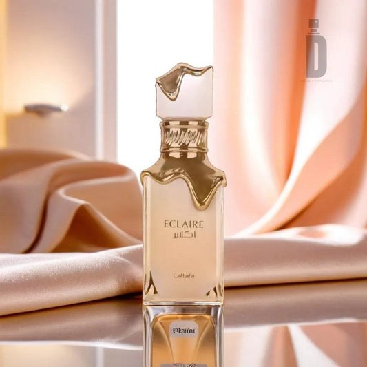A sleek perfume bottle labeled "Eclaire 100ml EDP - Lattafa," featuring a gold cap that evokes the image of liquid gracefully pouring down. The bottle is placed on a reflective surface, enhanced by soft, draped pink fabric in the background, creating an elegant and luxurious ambiance with hints of vanilla praline.