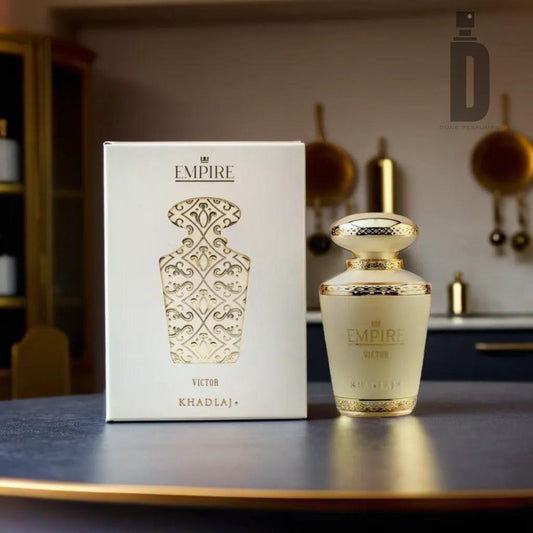 A luxurious Empire Victor 100ml EDP by Khadlaj sits beside its ornate box on a dark surface, against a blurred kitchen backdrop with gold accents and hanging utensils that evoke a warm vanilla aura.