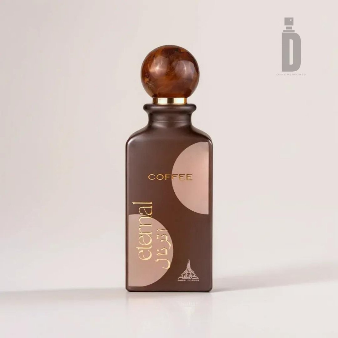 A rectangular perfume bottle in a dark brown shade with a wooden cap features the label "Eternal Coffee 85ml EDP - Paris Corner" and "COFFEE," along with text in another language, suggesting creamy sweetness. The background is plain and light in color.
