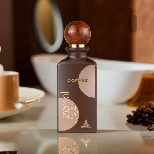 An 85ml bottle of "Eternal Coffee" Eau de Parfum by Paris Corner, adorned with gold and Arabic text, stands on a reflective surface. The brown bottle features a circular cap made of wood-like material. To the left is a coffee cup on a saucer, while scattered coffee beans in the foreground evoke its creamy sweetness and rich coffee fragrance.