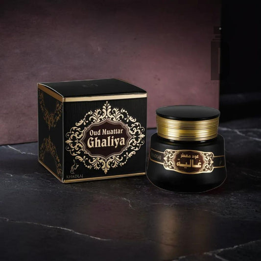 A decorative black box and matching jar labeled "Ghaliya Bakhoor 35g - Khadlaj" sit on a dark surface. The luxurious packaging features intricate gold detailing and Arabic calligraphy, adding an elegant touch of opulence and elegance. The brand name, Khadlaj, is visible on the packaging.