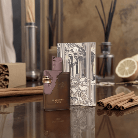 A bottle of Paris Corner's Gladiator's Oath 100ml EDP stands on a reflective surface beside its illustrated box, with cinnamon sticks, lemon slices, and decorative items softly blurred in the background.