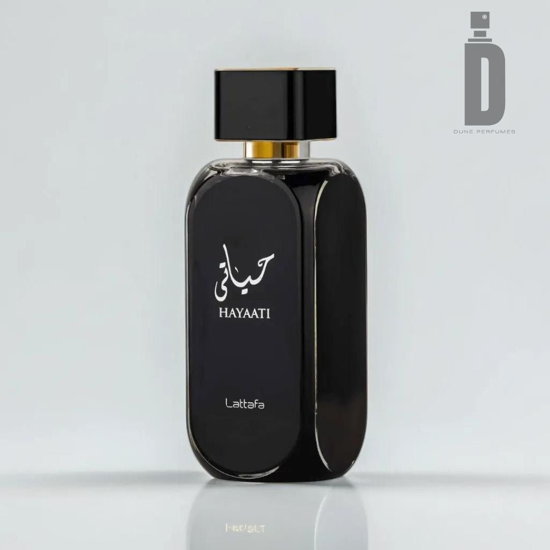 A black perfume bottle labeled "Hayaati 100ml EDP - Lattafa" stands against a plain white background. The sleek design, highlighted by a gold-accented neck and square black cap, exudes elegance. The logo "Dune Perfumes" appears in the top right corner, framing this exquisite fragrance as a must-have in your collection.
