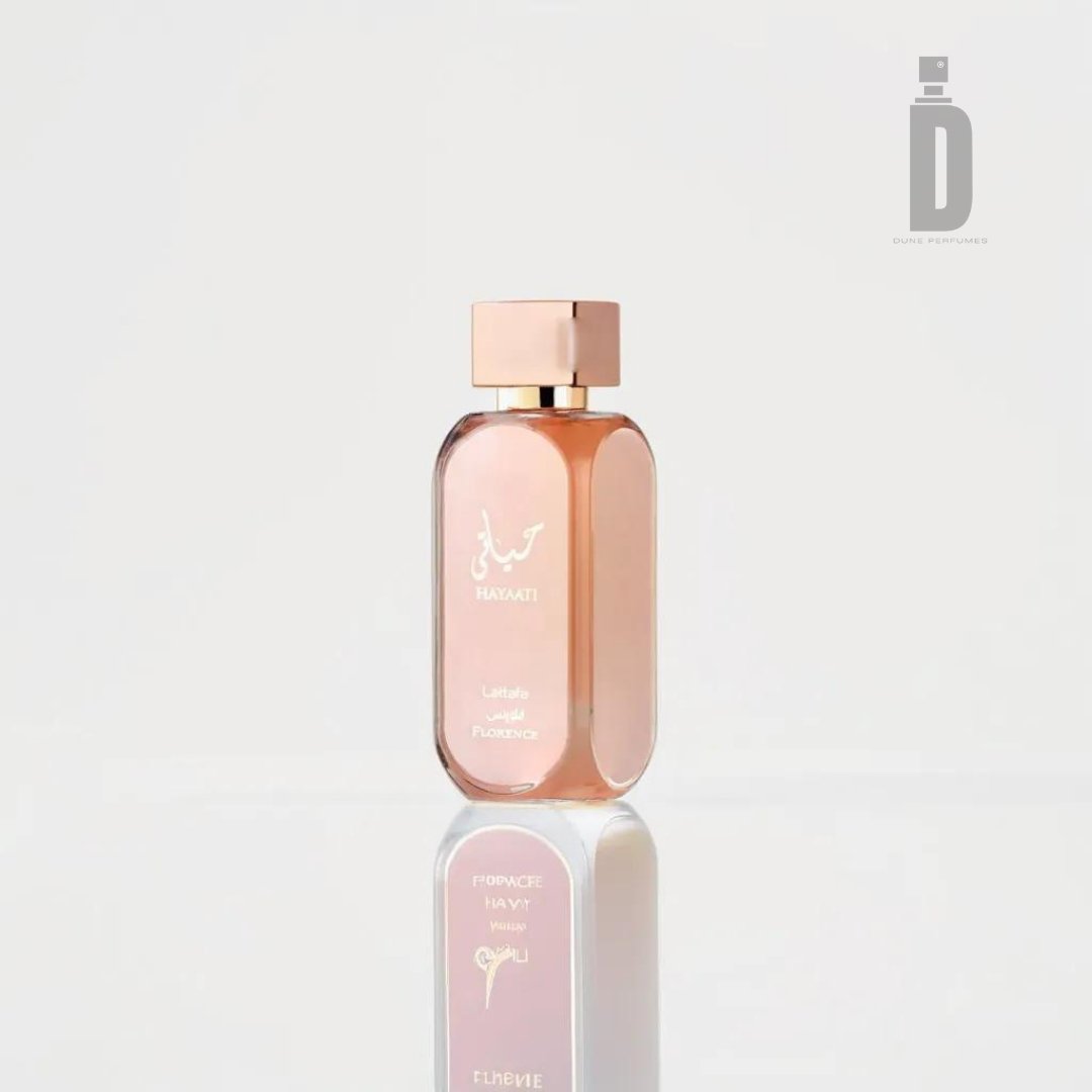 A transparent perfume bottle with a gold cap and gold lettering stands against a plain white background. The fragrance, labeled "Hayaati Florence 100ml EDP - Lattafa" in both Arabic and English, reflects exquisite Italian craftsmanship. Additional smaller text appears underneath, with the Lattafa logo in the upper right corner.