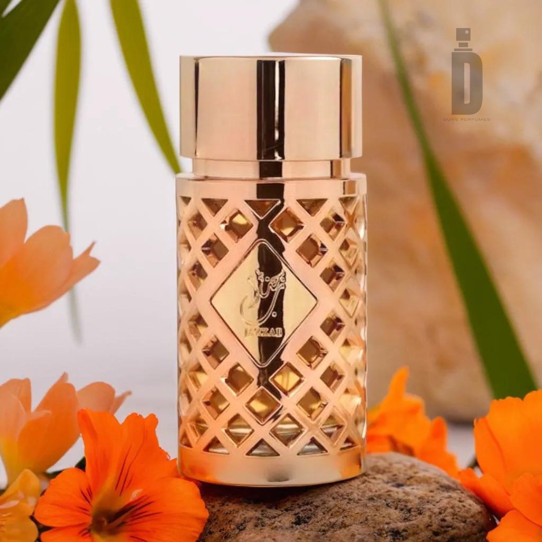 A gold, ornate perfume bottle with a lattice design sits on a stone slab, surrounded by bright orange flowers and green foliage. In the background, a large rock and part of a blurred leaf are visible. The sophisticated scent of Jazzab Gold 100ml EDP by Ard Al Zaafaran emanates from this luxurious fragrance container.