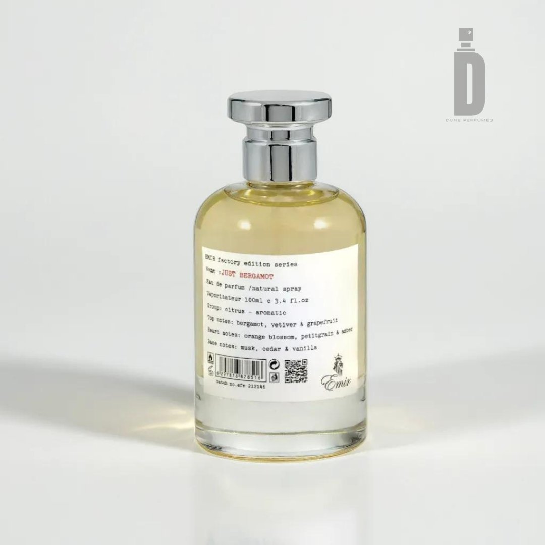 A cylindrical glass bottle with a silver cap contains a light yellow liquid, labeled as "Just Bergamont 100ml EDP - Emir" by Paris Corner. This Italian luxury fragrance showcases notes of citrus, bergamot, vetiver, and more. The Emigré logo graces the bottom alongside a small barcode.