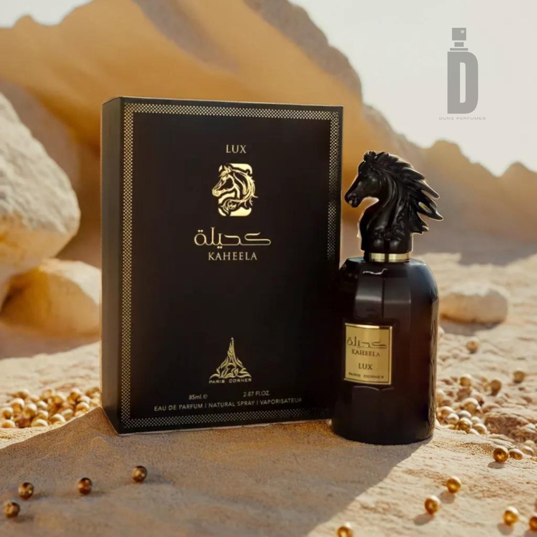 A perfume bottle with a horse-head cap sits next to a black and gold box labeled "Kaheela Lux 85ml EDP - Paris Corner" against a desert backdrop. Small golden beads are scattered on the sandy surface in the foreground, evoking an opulent fragrance of unparalleled splendor from Paris Corner.