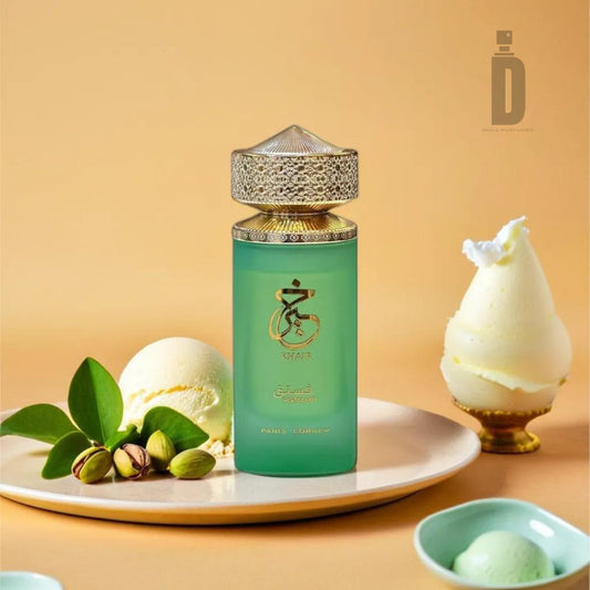 A green perfume bottle labeled Khair Pistachio 100ml EDP - Paris Corner, featuring an ornate golden cap, stands against a yellow background. The display is complemented by small bowls of pistachio-garnished ice cream and green leaves, crafting an elegant and refreshing visual that evokes the decadent fragrance of a gourmet dessert.
