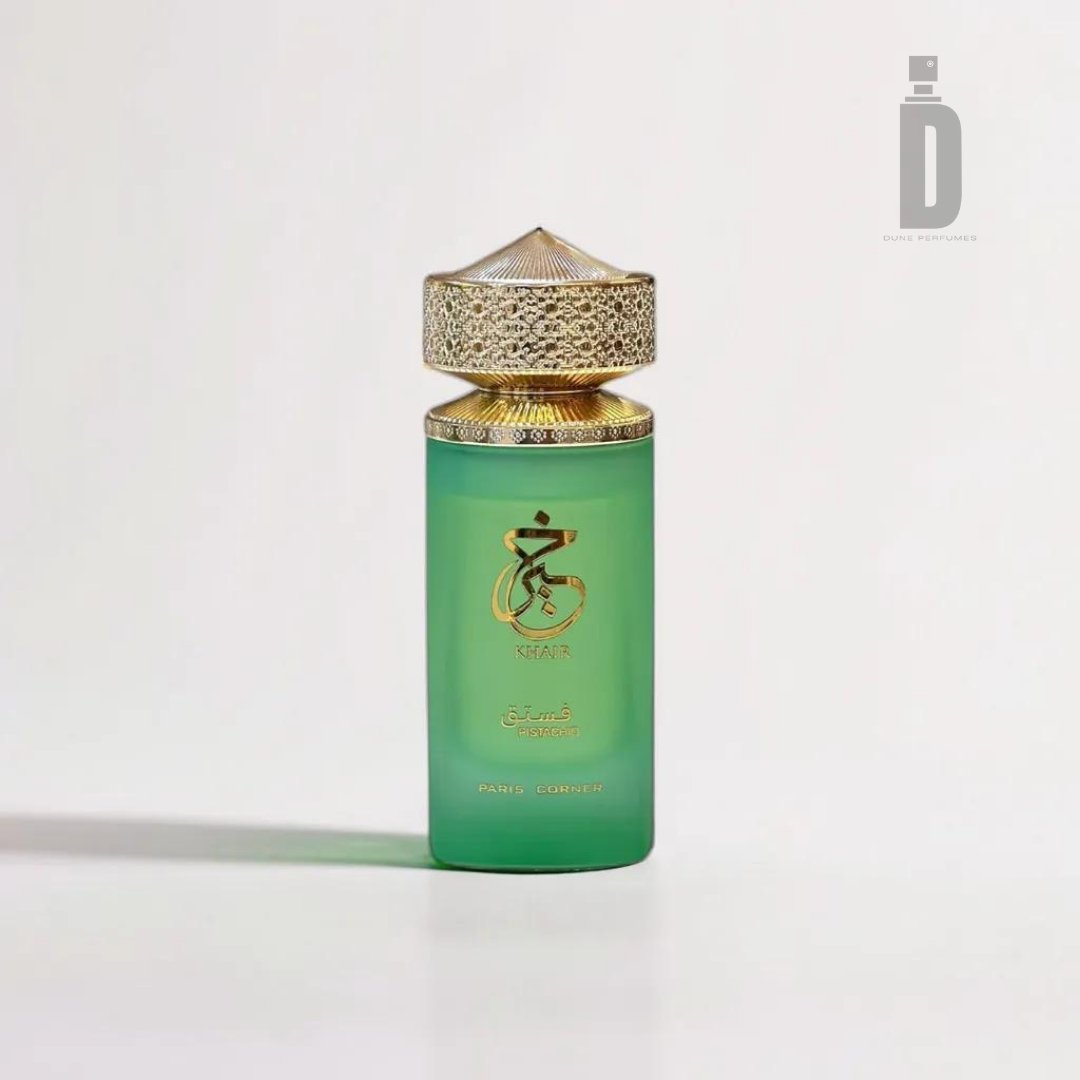 A green bottle of Khair Pistachio 100ml EDP by Paris Corner, adorned with an intricate golden cap and golden Arabic calligraphy on the front. The decadent fragrance evokes the allure of a gourmet dessert. The bottle is set against a plain white background, with a watermark featuring the letter "D" in the top right corner.