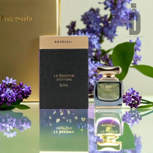 A luxurious fragrance set is displayed, featuring a bottle of Le Prestige Royal 100ML EDP by Khadlaj alongside its elegant packaging. The scene is enhanced by the presence of delicate purple flowers and a reflection on the glossy surface beneath.