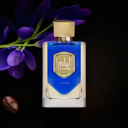 A bottle of perfume labeled "Liam Blue Shine 100ml EDP" in Arabic script, with "Lattafa" written below. The bottle contains a blue liquid that exudes invigorating freshness and has a gold cap. The background features a purple flower and a single coffee bean resting beside the bottle, adding to its magnetic allure.